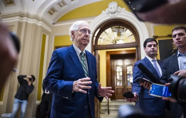 Idős férfi öltönyben újságíróknak nyilatkozik épületben