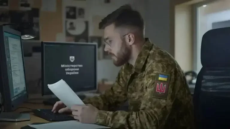 Ukrán egyenruhás férfi dokumentumot olvas számítógépnél