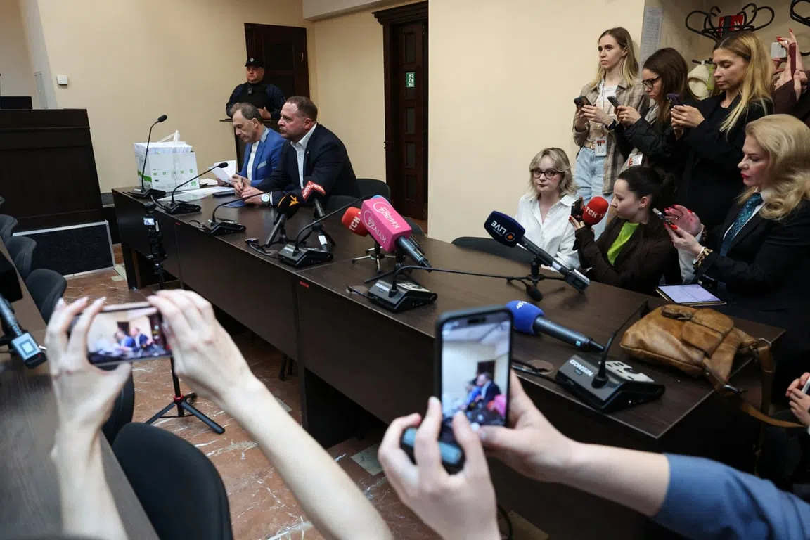 Sajtótájékoztató tárgyalóteremben újságírókkal és mikrofonokkal