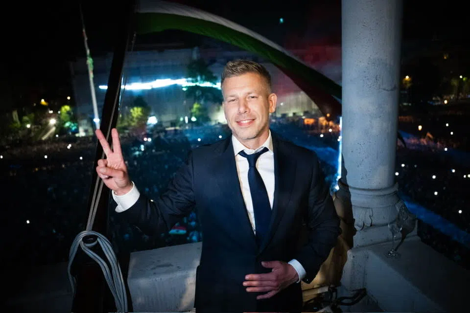Öltönyös férfi erkélyen, békejelet mutat éjjel